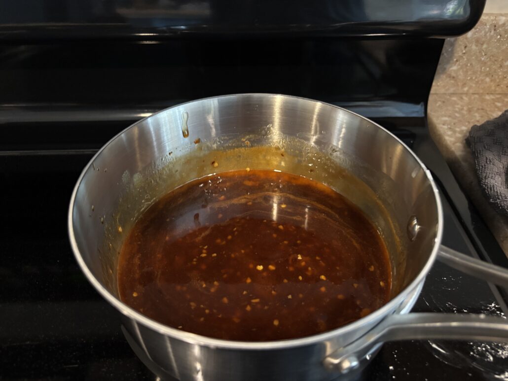 Wide view of the thickened honey soy glaze simmering in a saucepan on the stove