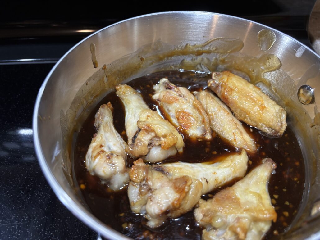 Freshly fried crispy chicken wings dropped into the hot sticky glaze in a pan