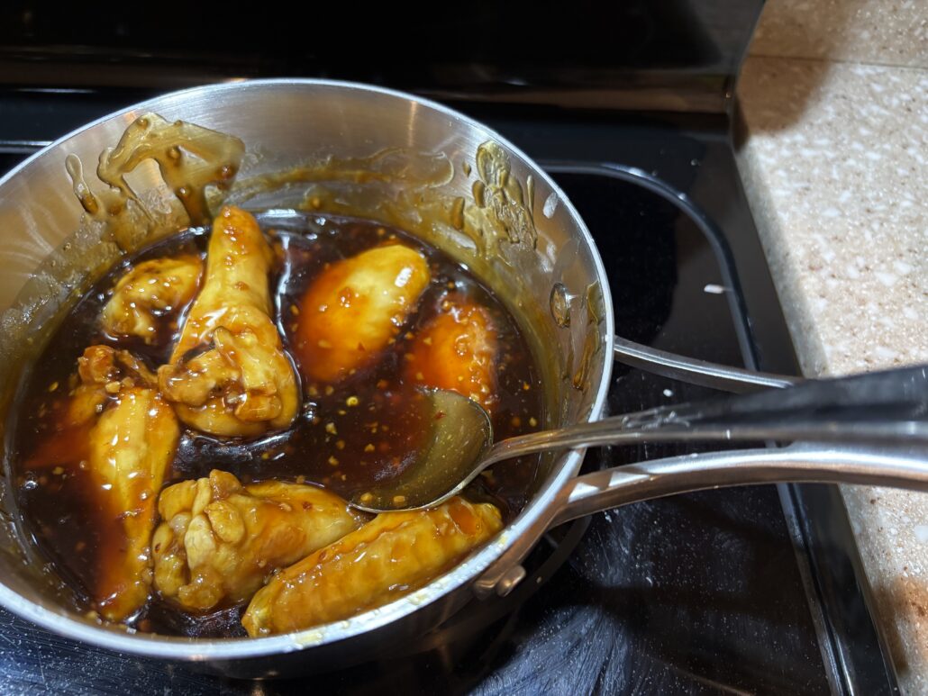 Sticky glazed chicken wings coated in dark honey soy sauce in a stainless steel pot
