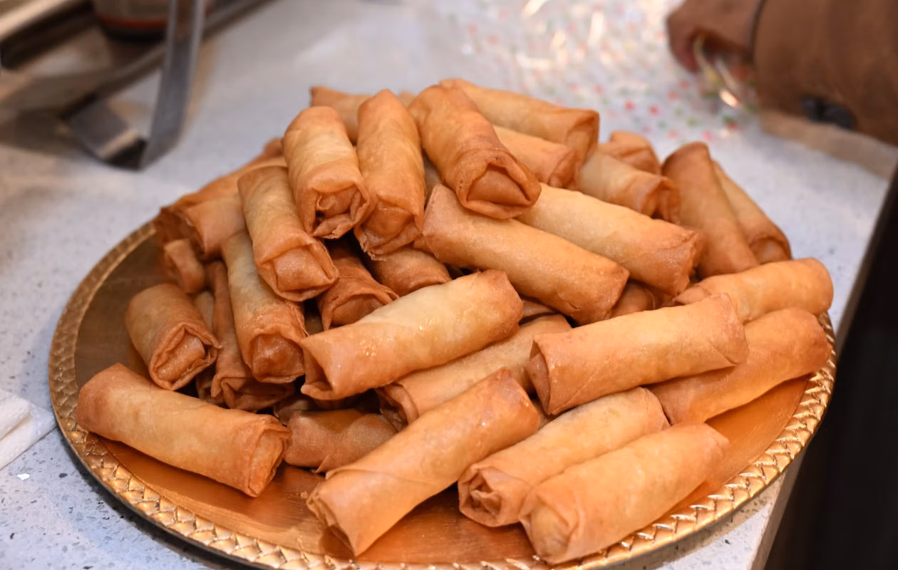 Bacon jam cheeseburger egg rolls stacked on a plate, golden and crispy after frying