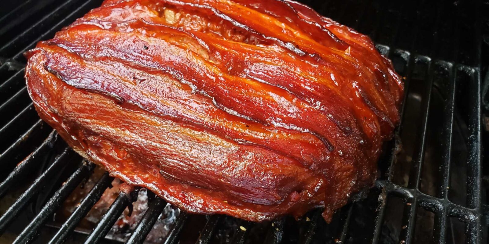 Smoked bacon-wrapped mac and cheese stuffed meatloaf on a pellet grill with a sticky BBQ glaze
